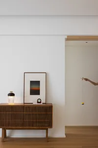 A modern living room featuring a wooden sideboard with a glass lamp, a framed picture, and a pendulum.