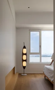A modern minimalist bedroom with wooden flooring, a large window, and a floor lamp