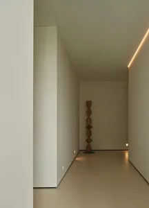 A minimalist hallway features a wooden sculpture and warm lighting.