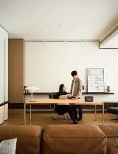 A man and a woman discussing in a modern minimalist living room with wooden furniture and a wooden desk.