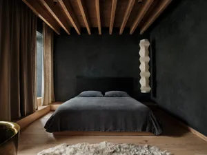 A minimalist bedroom with dark walls and wood flooring, featuring a low platform bed with a dark headboard and bedding, and a
