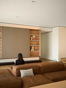 A minimalist living room with a brown leather sectional sofa and a wooden wall shelf.