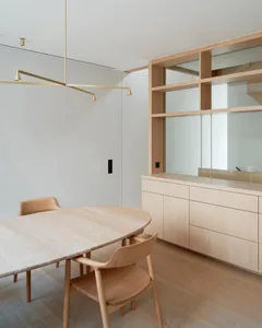 A minimalist living room with a light wood table and chairs, and a wall-mounted lamp.