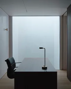 Minimalist office space featuring wooden desk and glass window with black chair.