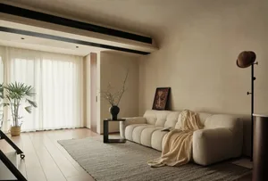 A minimalist living room with neutral-toned walls and soft furnishings on a beige rug, featuring a white sofa and a small bla