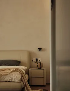 Minimalist bedroom featuring a neutral-toned bedside table with a vase and flowers.