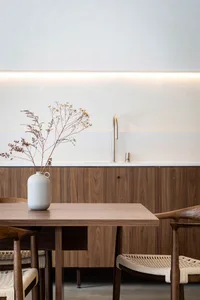 A minimalist residential kitchen with wooden furniture, a white vase with dried flowers, and a modern faucet in the backgroun
