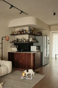 A modern residential kitchen featuring wood and metal materials with a bar counter and a white cat exploring a candle on a ru