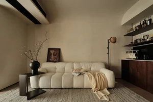 Minimalist living room with a neutral color palette featuring a plush, textured sofa, wooden coffee table, and modern lightin