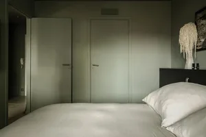 Minimalist bedroom with neutral tones, featuring a large bed, white pillows, and two green doors.