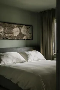 A minimalist bedroom with soft textiles and natural materials, featuring a bed with white bedding and wooden headboard, and a