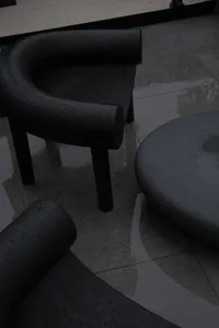 Black metal outdoor furniture with curved armrests and legs on a wet tiled floor.