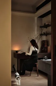 A minimalist home office featuring dark wood furniture and a cozy reading nook with a lit candle.