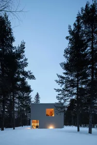 A minimalist residential building with metal cladding in a snowy forest setting.