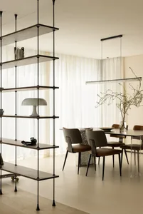 A modern dining room with wooden furniture, a long table, and chairs, featuring a shelf with a lamp and decorative items.