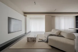A minimalist living room with a neutral color palette, featuring a large white sofa, a marble coffee table, and a flat-screen