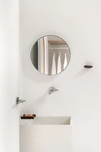 Circular mirror, sink, faucet, and soap dish in a minimalist bathroom setting.