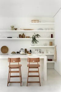 A minimalist interior with a white space, wooden chairs, and floating shelves.