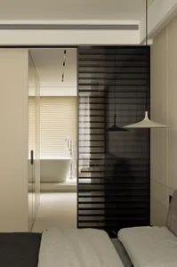 Modern living room with a sliding glass door transitioning into a bathroom with black frame and wooden furniture.