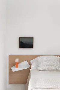 Modern bedroom with minimalist design featuring a floating wooden nightstand, white bedding, and an orange table lamp.