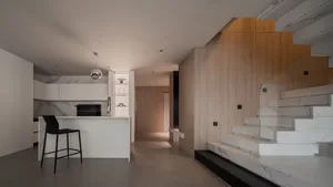 Modern residential interior with marble kitchen island, wooden stairs and wall, and geometric lighting fixture