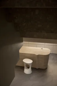 A modern, minimalist furniture set made of sandstone, featuring a sleek, organic-shaped table and a matching stool with a cut