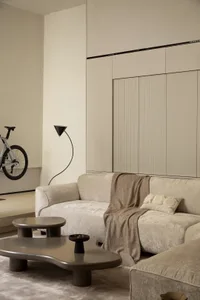 A minimalist living room with neutral-toned couches, coffee table, and bicycle wall-mounted.