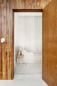 Minimalist bedroom featuring wooden walls and white bedding with a vase of flowers on a small table.