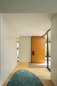 Minimalist entryway with hardwood flooring and wooden door, featuring a light blue rug and a window with white trim.
