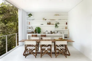 Modern dining room with light wooden table and chairs, ceramic shelving, and green plants