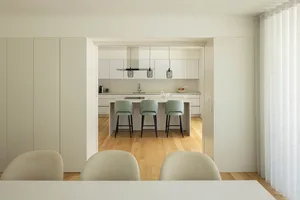 Modern kitchen featuring white cabinets, countertop, and bar stools with green accents.