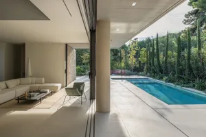 A modern living room with a concrete floor and furniture overlooking a pool and garden.