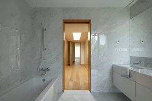 A minimalist bathroom with marble walls and a white bathtub.