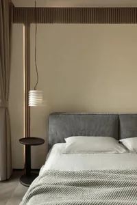 Minimalist bedroom featuring a gray upholstered headboard and textured bedding, set against a beige wall and floor with ambie