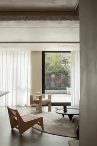 A minimalist living room featuring a brown wooden chair, a black low table, a beige upholstered chair, and a large window wit