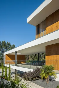 Contemporary house with wooden and glass exterior, featuring concrete patio and greenery.