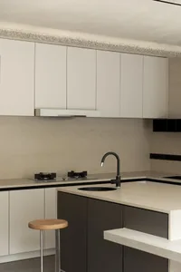 Modern kitchen featuring concrete countertops with black fittings and a wooden stool.