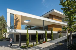 A modern residential exterior featuring a combination of white concrete, glass, and wood materials.