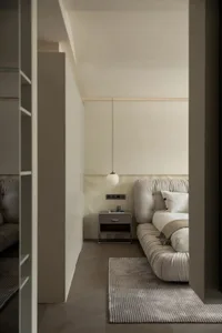 A minimalist bedroom featuring neutral-toned furnishings and a hanging pendant light.