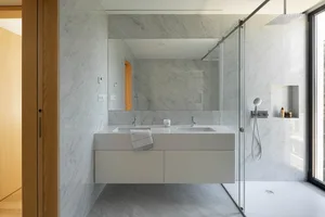 Contemporary marble bathroom with white porcelain sinks, white doors, and glass shower enclosure.