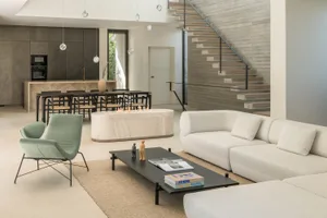 A minimalist living room featuring a concrete staircase, marble fireplace, and white furniture.
