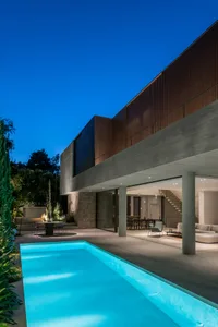 A modern house featuring a concrete, glass, and wooden exterior with a swimming pool and outdoor seating area.