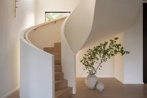 A modern minimalist staircase with a curved white handrail and wooden steps.