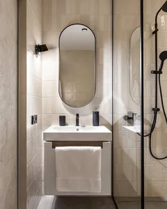 Minimalist bathroom with modern fixtures, oval-shaped mirror, and white ceramic tiles on walls and floor.