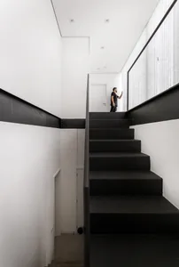 A modern staircase with black steps and a white wall in a minimalist architectural design.