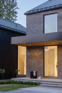 Contemporary brick house with large windows and a metal roof, image taken during twilight.