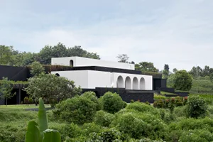 A modern house with black and white exteriors surrounded by lush greenery and trees in a wilderness setting.