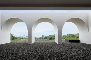 A view through an arched corridor of a modern interior with a concrete floor and natural landscape outside.