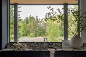 A modern kitchen with a marble countertop and sink overlooking a forested landscape.