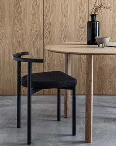 Modern minimalist dining area featuring a wooden table with black legs and a black upholstered chair with a black vase on top